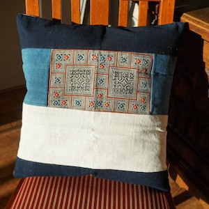 May include: A blue and white patchwork pillow with a geometric design in the center. The pillow is sitting on a red and white striped chair.
