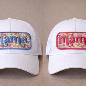 Pode incluir: Duas bonés brancos de caminhoneiro com um patch floral que diz "mama". Um boné tem letras azuis, o outro rosa. Os patches retangulares apresentam um design floral e uma borda colorida.