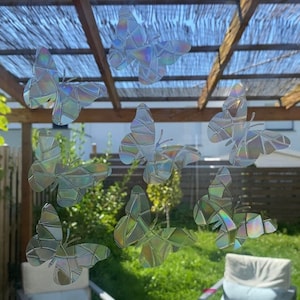 May include: A set of iridescent butterfly window clings, featuring a mosaic-like design. The clings are applied to a glass window, with a view of a patio and lush greenery behind them.