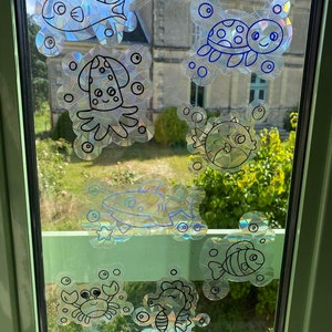 Può includere: Un set di otto adesivi per finestre iridescenti con diverse creature marine, tra cui un pesce, un polpo, una tartaruga, un pesce palla, uno squalo, un cavalluccio marino, un granchio e un pesce pagliaccio. Gli adesivi sono contornati di nero e hanno un effetto olografico scintillante.