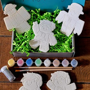 May include: A craft kit with the text "Happy Painting" on the box. The kit includes several unpainted character figures, paint pots, brushes, and glitter. The figures are in a box with green filler.