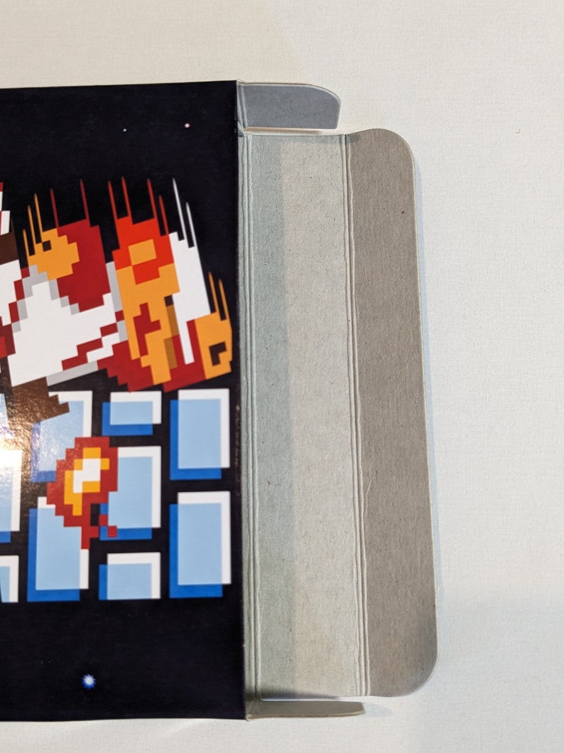 Pu&ograve; includere: Una scatola di cartone con un personaggio di videogioco sul davanti. Il personaggio &egrave; in stile pixelato e indossa un abito rosso e bianco. Il personaggio sta saltando e ci sono delle fiamme dietro di lui. La scatola &egrave; piegata e i bordi sono visibili.