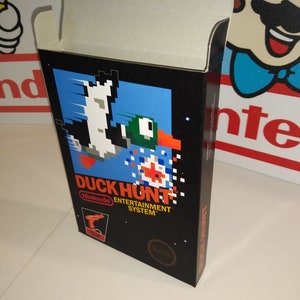 May include: A black Nintendo Entertainment System game box with a blue and white pixelated image of a duck and a gun. The game title is "Duck Hunt" and the Nintendo logo is visible on the bottom right corner.