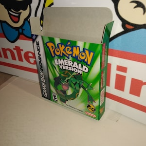 May include: A green Game Boy Advance game cartridge case for Pokemon Emerald Version. The case is open and shows the game cartridge inside. The front of the case features a green background with a white Pokemon logo and the words "Emerald Version" in white text. The back of the case features a green background with white text.