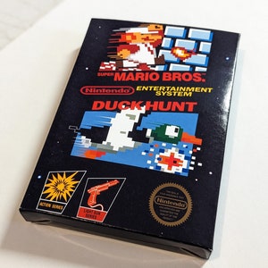 Pu&ograve; includere: Una cartuccia di gioco nera per Nintendo Entertainment System per Duck Hunt, con un'immagine pixelata di un'anatra e un cane sul davanti. Il gioco fa parte della serie Action e utilizza una pistola luminosa.