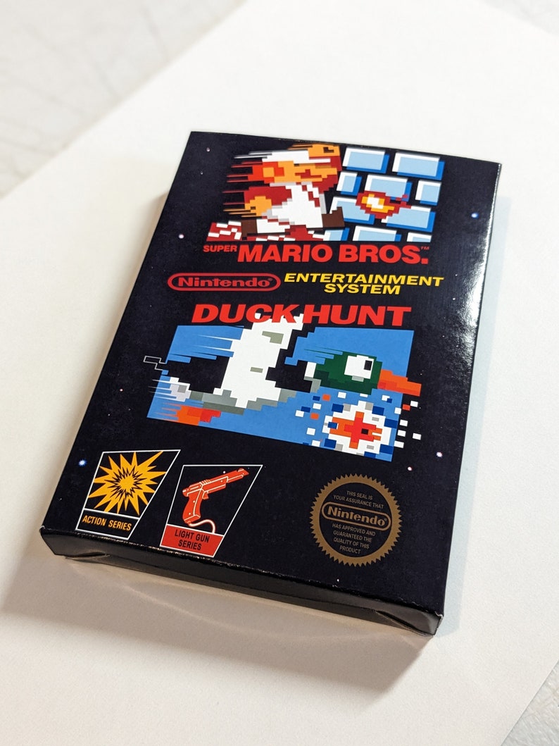 Pu&ograve; includere: Una cartuccia di gioco nera per Nintendo Entertainment System per Duck Hunt, con un'immagine pixelata di un'anatra e un cane sul davanti. Il gioco fa parte della serie Action e utilizza una pistola luminosa.