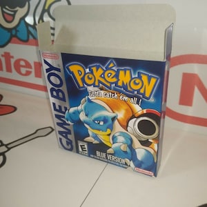May include: A blue Game Boy Color game cartridge box for Pokemon Blue Version. The box features a blue and orange Pokemon character with the text "Gotta catch 'em all!" and "Blue Version".
