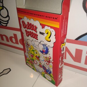 May include: A red and white Nintendo Entertainment System game cartridge box for Bubble Bobble Part 2. The box features a colorful illustration of the game's characters, including the main character, a green bubble-blowing creature, and a blue monster.