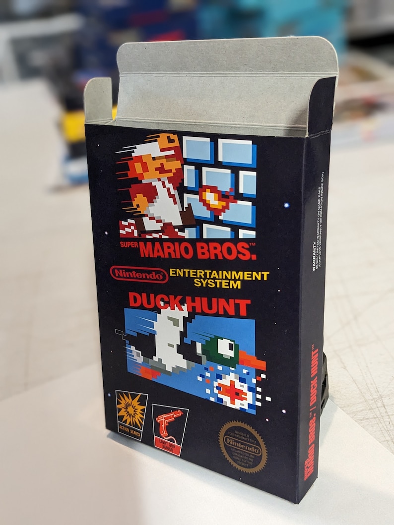 Pu&ograve; includere: Una cartuccia di gioco vintage per Nintendo Entertainment System per Duck Hunt, con uno sfondo nero e un'immagine pixelata di un'anatra che vola via da un bersaglio rosso. La cartuccia di gioco &egrave; etichettata "SUPER MARIO BROS.TM" e "DUCK HUNT" in testo bianco.