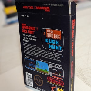 Pu&ograve; includere: Una scatola di gioco nera per Nintendo Entertainment System per Super Mario Bros./Duck Hunt. La scatola presenta un'immagine rossa e bianca di Mario e un'anatra. Il retro della scatola mostra schermate del gioco e istruzioni per giocare. Il testo sulla scatola recita "Super Mario Bros./Duck Hunt".