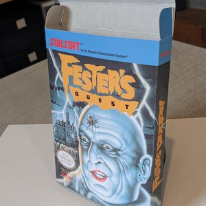 May include: A vintage video game box for "Fester's Quest" for the Nintendo Entertainment System. The box features a blue-skinned character with a spider on his head, a haunted house, and lightning bolts. The Sunsoft logo is visible.