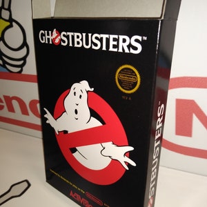 Può includere: Una scatola di videogiochi nera e rossa per il Nintendo Entertainment System. La scatola presenta il logo dei Ghostbusters con un fantasma nel simbolo "no ghost". Il testo sulla scatola recita "Ghostbusters" e "Licensed by Nintendo for play on the Nintendo Entertainment System. Activision."