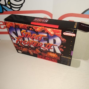 May include: A Super Nintendo game box for Street Fighter II. The box is black with red and white accents. The game title is printed in large, white letters. The box is in good condition.