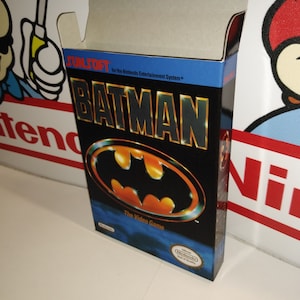 Op de afbeelding: Een zwarte en blauwe Nintendo Entertainment System-spelcartridge doos voor het spel Batman: The Video Game. De doos heeft een groot beeld van het Batman-logo met een geel vleermuissymbool. De tekst "Sunsoft" en "Batman" staat in gele letters op een blauwe achtergrond.