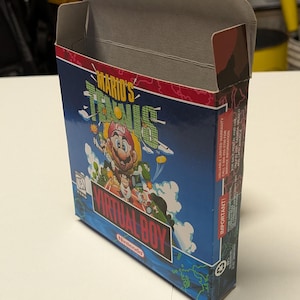 Könnte beinhalten: Geöffnete Pappschachtel für das Nintendo Virtual Boy-Spiel "Mario's Tennis". Die Schachtel hat einen blauen Hintergrund mit Mario und anderen Charakteren. Der Text "VIRTUAL BOY" und "Nintendo" sind sichtbar.