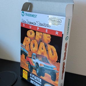以下が含まれることがあります： Nintendo Entertainment System用ビデオゲーム「Ivan Ironman Stewart's Super Off Road」の長方形の紙製ボックス。前面は白、赤、黒のデザインで、トヨタのトラック、タイトルテキスト、「4 player action」の文字が描かれています。