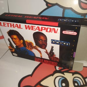 May include: A Super Nintendo game box for "Lethal Weapon" featuring Mel Gibson and Danny Glover. The box has a black background with the Ocean and Nintendo logos. The title is in red.