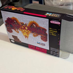 Könnte beinhalten: Super Nintendo-Spielbox für das Spiel "VARRUN". Die Box zeigt eine detaillierte Illustration eines mechanischen Widders mit dem Spieltitel. Die Box hat einen schwarzen Hintergrund mit weißen Leiterplattenlinien und dem Text "Life on the cyberpunk fringe of the future..."