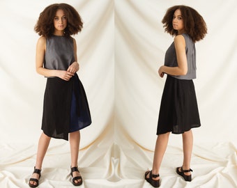 May include: A woman is wearing a gray sleeveless linen top and a black and blue linen wrap skirt. She is wearing black sandals.