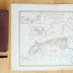 Op de afbeelding: Een donkerrood hardcover boek met de titel Schillers ausgewählte Werke, een zwarte vulpen en een grote, rechthoekige, vintage papieren kaart van de Middellandse Zee met gedetailleerde geografische lijnen en Duitse tekst.