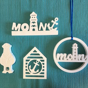 Könnte beinhalten: Weiße Ornamente und Dekorationen zum Thema Nautik. Enthält zwei Möwenfiguren, ein Schild mit dem Wort "MOIN" und einem Anker, ein hausförmiges Ornament mit einem Anker und ein rundes Ornament mit einem Leuchtturm und dem Wort "moin".