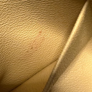 May include: Close-up of a light yellow leather interior with a textured surface. The leather has a subtle grain pattern and a small, reddish-brown stain. The image shows the inside of a wallet or similar item.