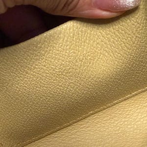 May include: Close-up of a light yellow leather interior. The embossed text "LOUIS VUITTON PARIS" is visible. The leather has a textured surface.