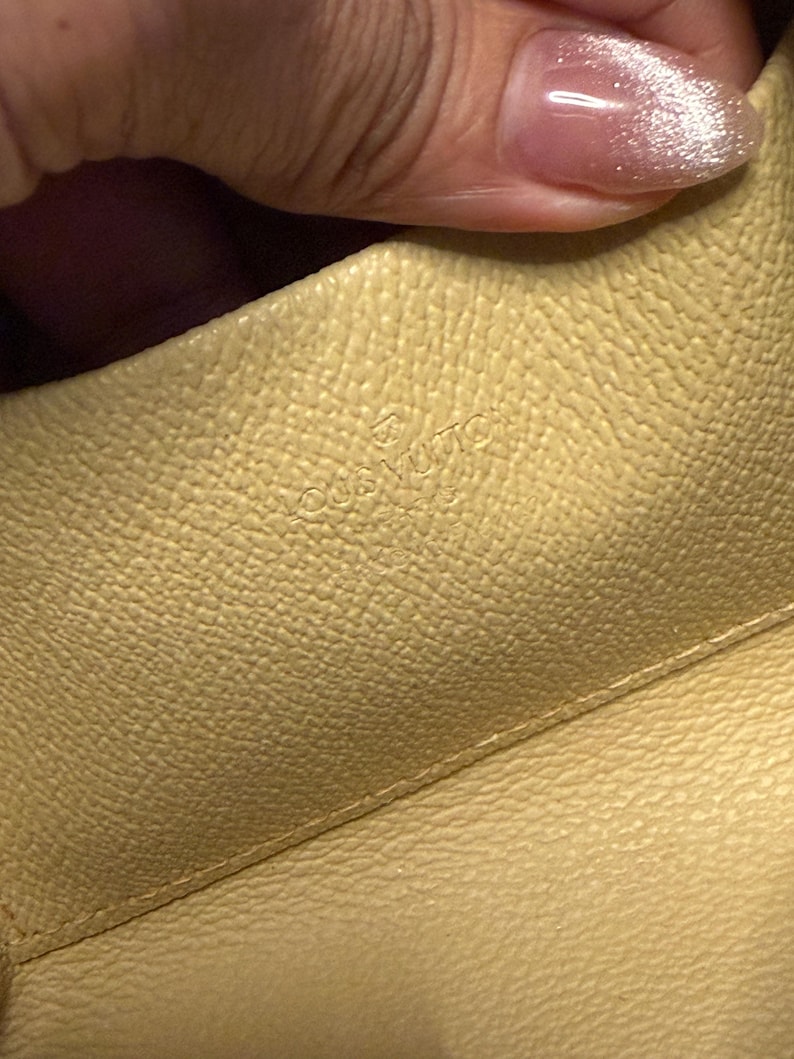 May include: Close-up of a light yellow leather interior. The embossed text "LOUIS VUITTON PARIS" is visible. The leather has a textured surface.