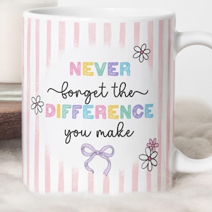 Può includere: Tazza in ceramica bianca con sfondo a righe rosa e la scritta "NEVER forget the DIFFERENCE you make" a lettere colorate. La tazza è decorata con illustrazioni di fiori e fiocchi.