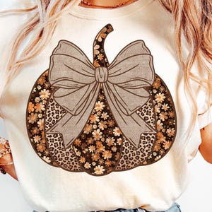 May include: Cream-colored sweatshirt featuring a large pumpkin design. The pumpkin has a brown bow, floral and leopard print details. The text "PNG - INSTANT DOWNLOAD" is at the bottom of the image. A fall-themed graphic.