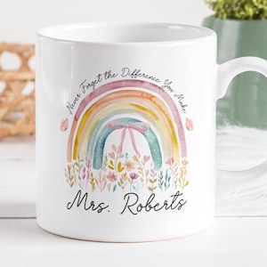 Può includere: Tazza in ceramica bianca con un design ad arcobaleno ad acquerello e la scritta "Never Forget the Difference You Make" e "Mrs. Roberts". La tazza ha un manico curvo ed è decorata con fiori e farfalle.
