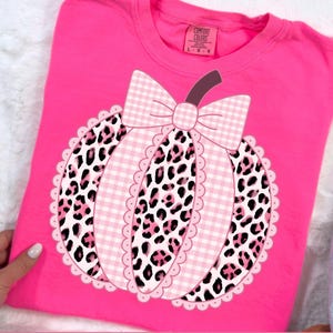 May include: A vibrant pink t-shirt with a pumpkin design. The pumpkin features a pink gingham bow, leopard print sections, and a scalloped edge. The shirt has the text "PNG - INSTANT DOWNLOAD" at the bottom.