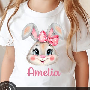 May include: A white t-shirt with a pink bunny rabbit with a pink bow. The bunny has big brown eyes and a pink nose. The name Amelia is written in pink letters below the bunny.