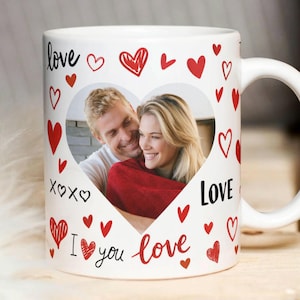 May include: White ceramic mug featuring a heart-shaped photo frame with a couple inside. The mug is decorated with red hearts and the words "love," "xoxo," and "I love you." A perfect gift for Valentine's Day or any romantic occasion.