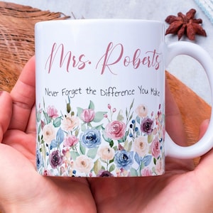 Può includere: Tazza in ceramica bianca con un design floreale e la scritta "Mrs. Roberts" in corsivo rosa. La tazza presenta anche la frase "Never Forget the Difference You Make". Il fondo della tazza è decorato con un bordo floreale colorato.