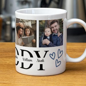 Puede incluir: Una taza de cerámica blanca con dos paneles fotográficos rectangulares que muestran personas, el texto grande en negro DADDY, los nombres Sophia, William y Noah en letra cursiva y tres corazones azules dibujados a mano en el lado del asa.