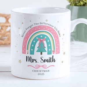 Può includere: Tazza in ceramica bianca con un design arcobaleno, un albero di Natale e la scritta "Never Forget The Difference You Make". La tazza è personalizzata con "Mrs. Smith" e "Christmas 2025."