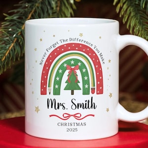 Può includere: Tazza in ceramica bianca con un design natalizio. La tazza presenta un arcobaleno con un albero di Natale, il testo "Never Forget The Difference You Make", il nome "Mrs. Smith" e la parola "Christmas" con l'anno 2025.