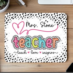 Puede incluir: Una alfombrilla de ratón rectangular blanca con un borde de lunares dálmata en blanco y negro. La alfombrilla presenta el nombre "Mrs. Stone" encima de la palabra "teacher" en letras coloridas. Las palabras "teach, love, inspire" están debajo.