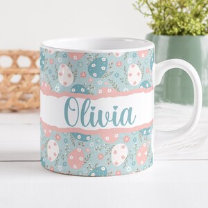 May include: White ceramic mug with a blue and pink Easter egg pattern and the name "Olivia" written in blue cursive.