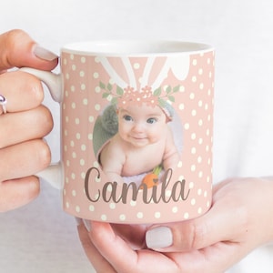 May include: A pink ceramic mug with white polka dots and a bunny rabbit design. The mug features a photo of a baby girl with a floral headband and the name "Camila" written in brown script.