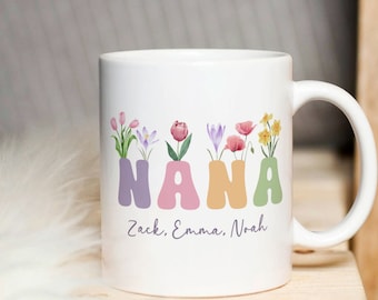 May include: White ceramic mug with a floral design spelling out "NANA" in colorful letters. The mug has a personalized message at the bottom that reads "Zack, Emma, Noah".