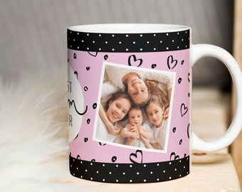 Puede incluir: Taza de cerámica blanca con fondo rosa y lunares negros. La taza presenta una foto de una familia de cuatro personas, incluyendo una madre y tres hijos, con corazones y puntos alrededor de la foto. El texto "Best Mom Ever" está escrito en la taza.