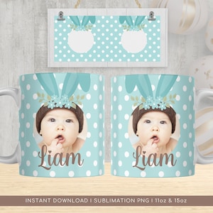 May include: A sublimation design for a 11oz or 15oz mug featuring a baby wearing a brown hat with bunny ears and a floral headband. The mug has a light blue background with white polka dots and the name "Liam" printed in brown.