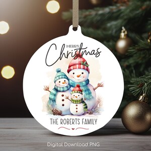 May include: A white round Christmas bauble featuring a watercolour illustration of three snowmen. The snowman family are wearing scarves and hats. The bauble has the text "Merry Christmas" and "The Roberts Family" printed on it.