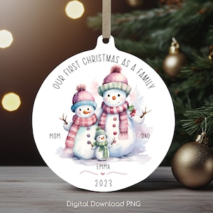 May include: A round Christmas ornament with a snowman family illustration. The text reads "OUR FIRST CHRISTMAS AS A FAMILY", with names "Mom", "Dad", and "Emma", and the year "2023". The ornament is white with a beige ribbon for hanging, and features a watercolor design.
