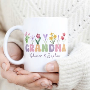 Pode incluir: Caneca de cerâmica branca com um design floral e a palavra "GRANDMA" em cores pastel. Os nomes "Oliver & Sophia" estão escritos abaixo da palavra "GRANDMA".