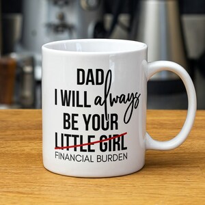 Puede incluir: Taza de cerámica blanca con texto negro que dice "Papá, siempre seré tu pequeña niña" con una línea roja sobre "niña" y las palabras "Carga financiera" debajo.