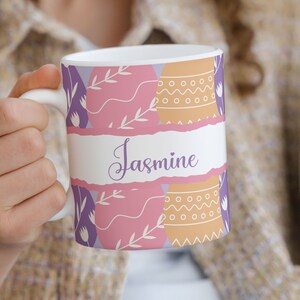 May include: White ceramic mug with a pink, purple, and orange Easter egg design. The mug has the name "Jasmine" written on it.