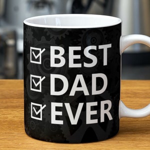 Może przedstawiać: Biały kubek ceramiczny z czarnym tłem i białym tekstem, który brzmi "BEST DAD EVER" z zaznaczonymi polami wyboru obok każdego słowa. Tło zawiera wzór zębatek.